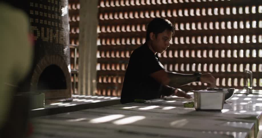 A man in a restaurant rolls out pizza dough