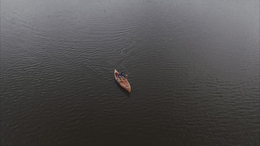 Light reflects on the ripples in the water as a man rows a canoe across the lake