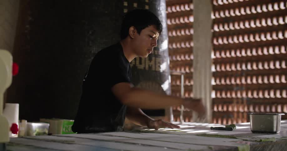Young man extends thin layers of dough over a table in the restaurant kitchen