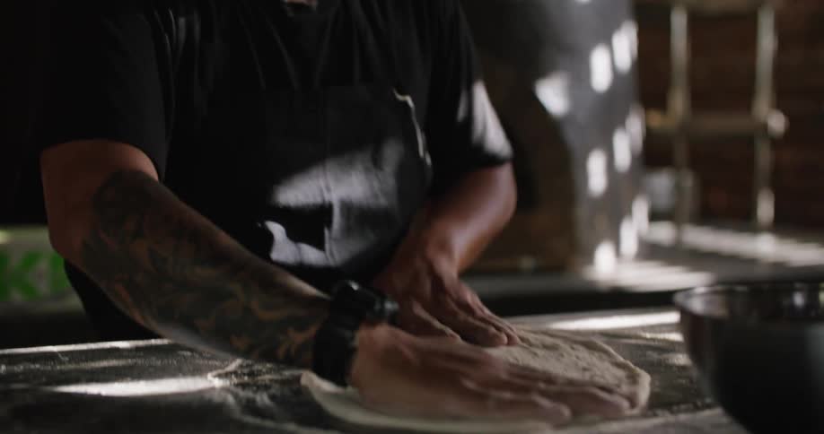 Man kneading dough for a pizza over the table in the restaurant kitchen
