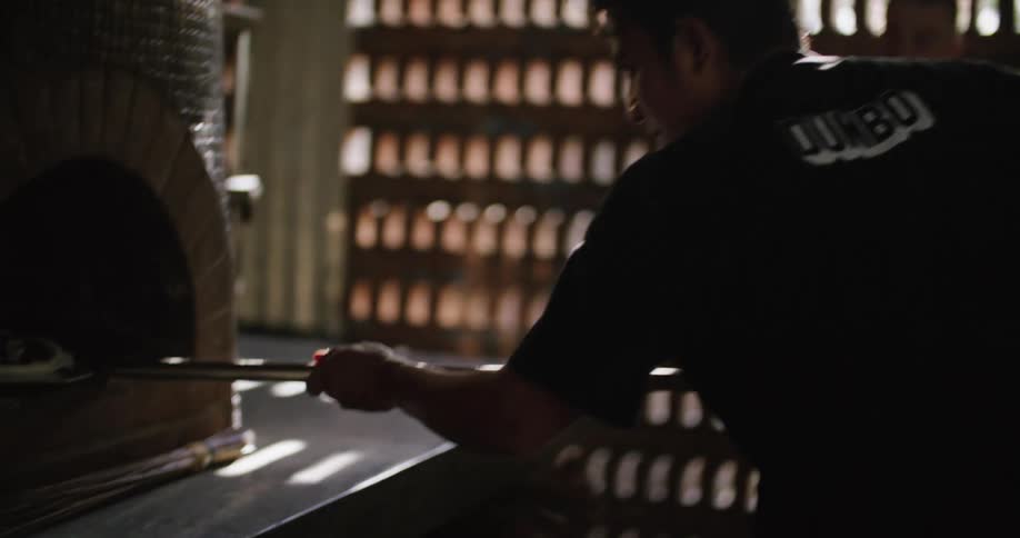 Man in hawaiian print shirt watches cook place pizza in pizza oven