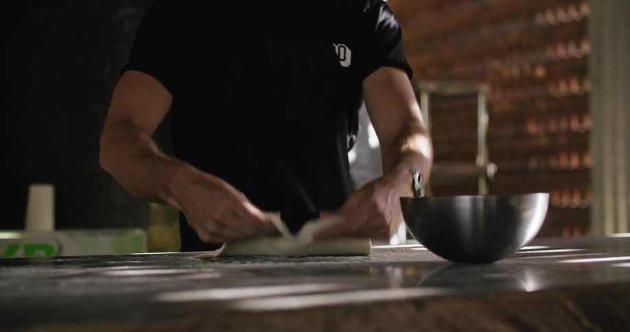 Man wearing apron works with dough on counter in restaurant