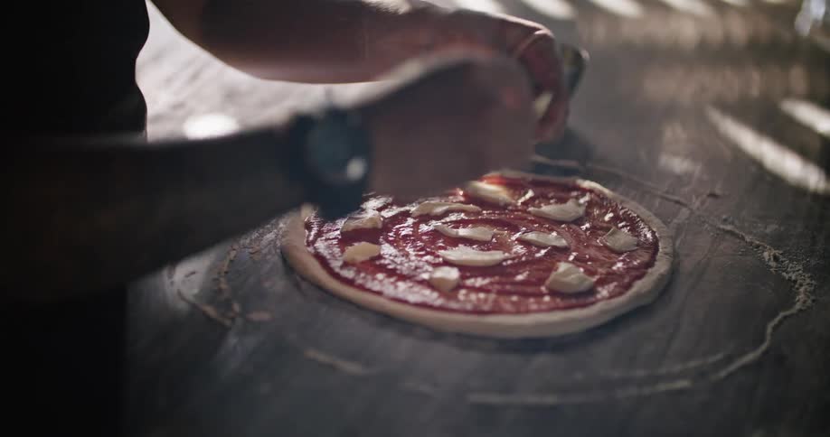 Man tops pizza dough and tomato sauce with cheese