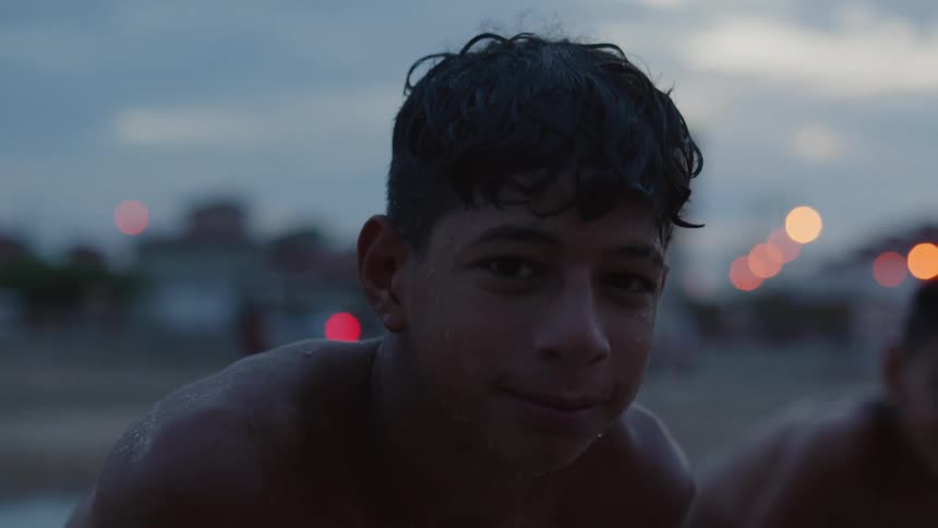Shirtless sweaty boy standing on a park near residential buildings at evening looking at the camera