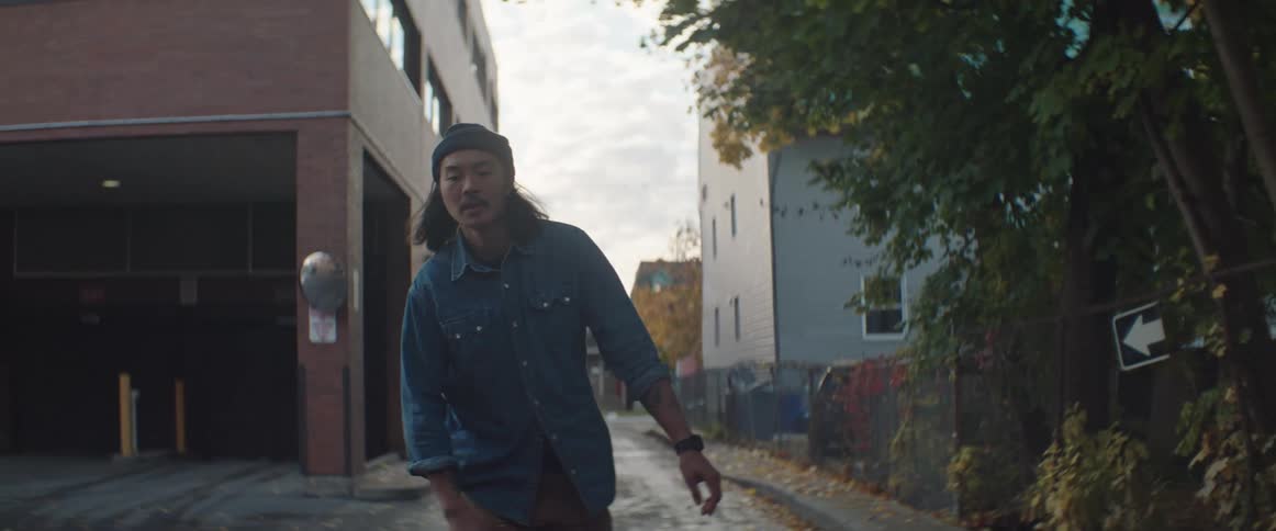 Long haired man rides a skateboard through an alley street in the morning