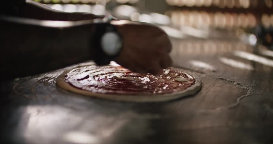 Man prepares a pizza over a table in a restaurant kitchen at morning