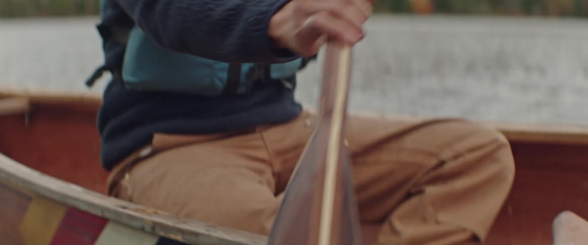 A man is holding an oar in the water and rowing a canoe
