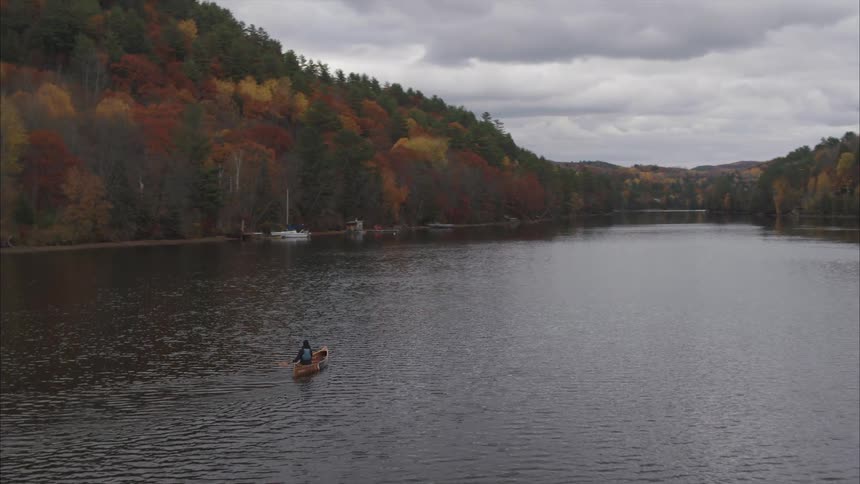 Aerial view of a man rowing a canoe on a lake near the forest in the mountains in the daytime