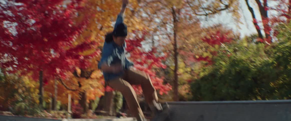 A man rides his skateboard on a ramp in a park among trees with bright fall colored leaves