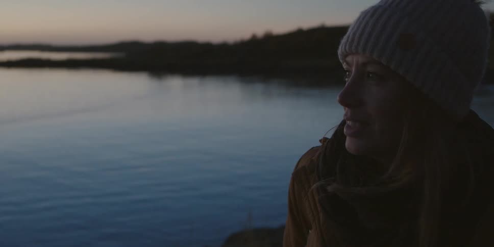 A woman walks along the shore of a lake at sunset