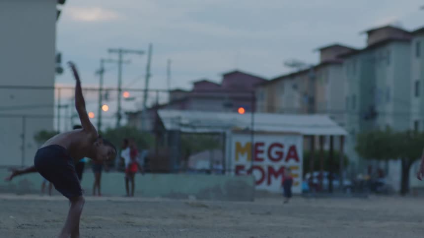 Shirtless boys playing soccer on a wet field near the residential buildings at evening