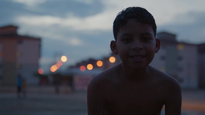A young boy leans forward and smiles at the camera while standing outside