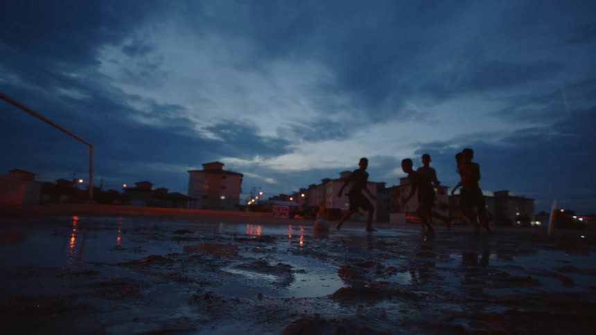 A group of boys are splashing in water puddles as they play soccer in the rain