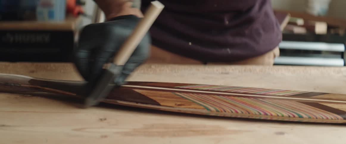 Man with tattoo seals woodwork art piece using sealant while standing in workshop