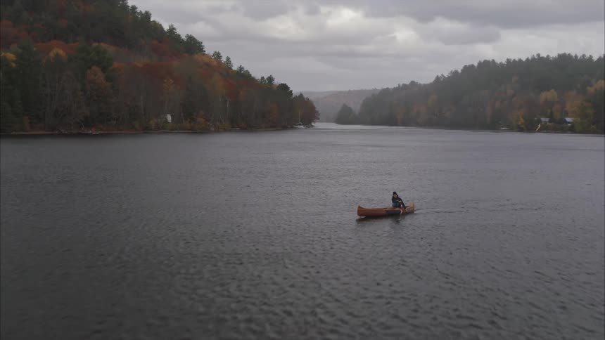 Aerial view of a man rowing a canoe on a lake with surrounding mountains during autumn