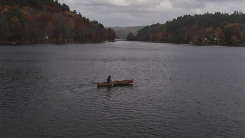 Aerial view of a man paddling a canoe on a lake during a cloudy day