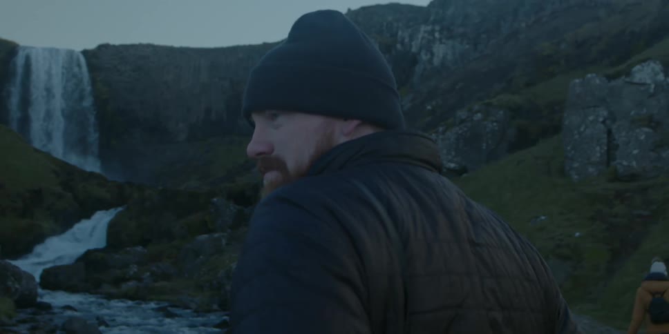 Big man looking at a waterfall turns around to look at the camera at morning