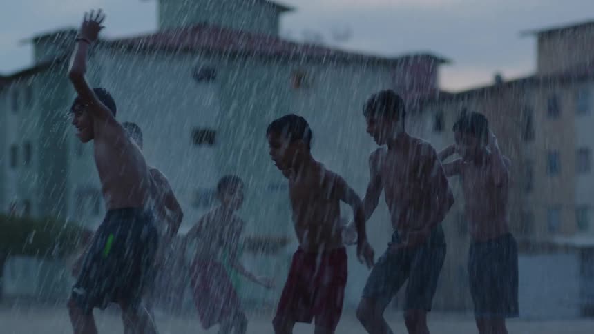 A group of boys are splashing in the water as they dance and jump in puddles in the rain
