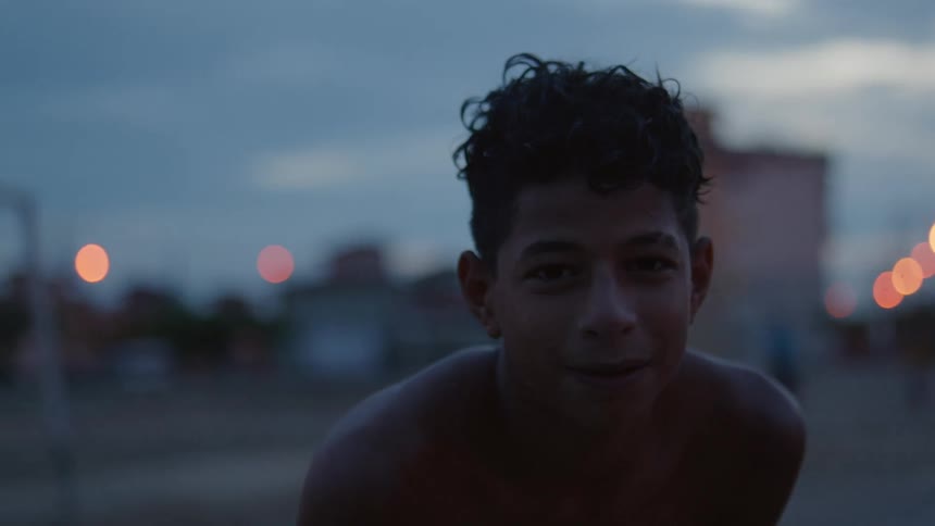 Young shirtless boy looking at the camera in front of apartment buildings at evening
