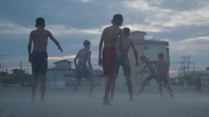 A group of boys are splashing in the water as they play soccer in the pouring rain and someone rides a bicycle near them