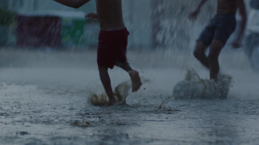 A group of boys are splashing in the water and mud as they play soccer in the pouring rain