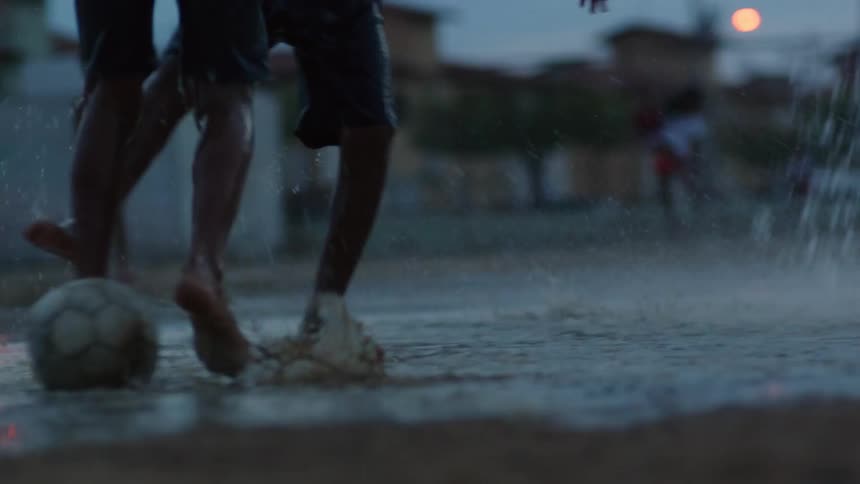 A group of boys are splashing in the water and mud as they play soccer in the rain