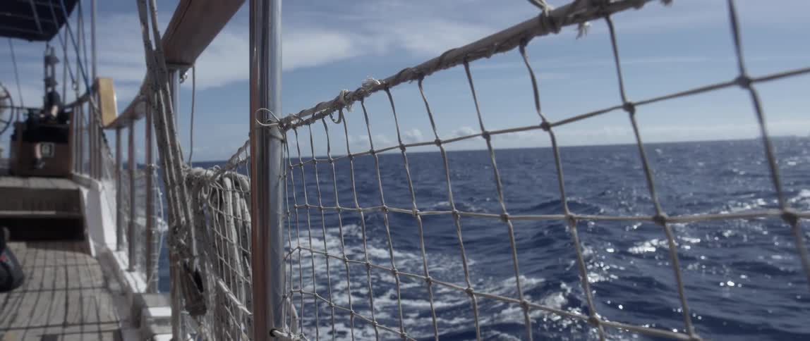 The ship's wake is seen through the railing of the ship as it sails