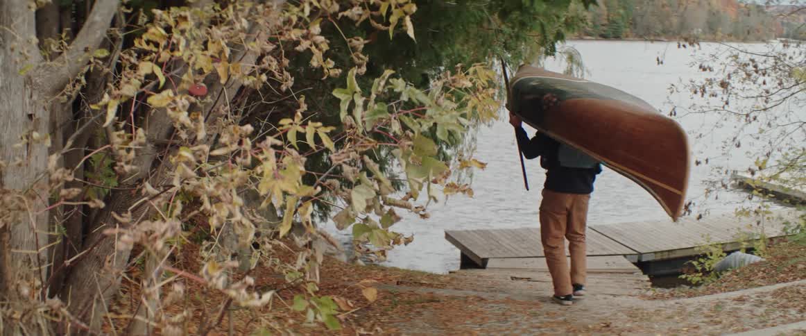 Man carries a boat over his head to a lakeside dock