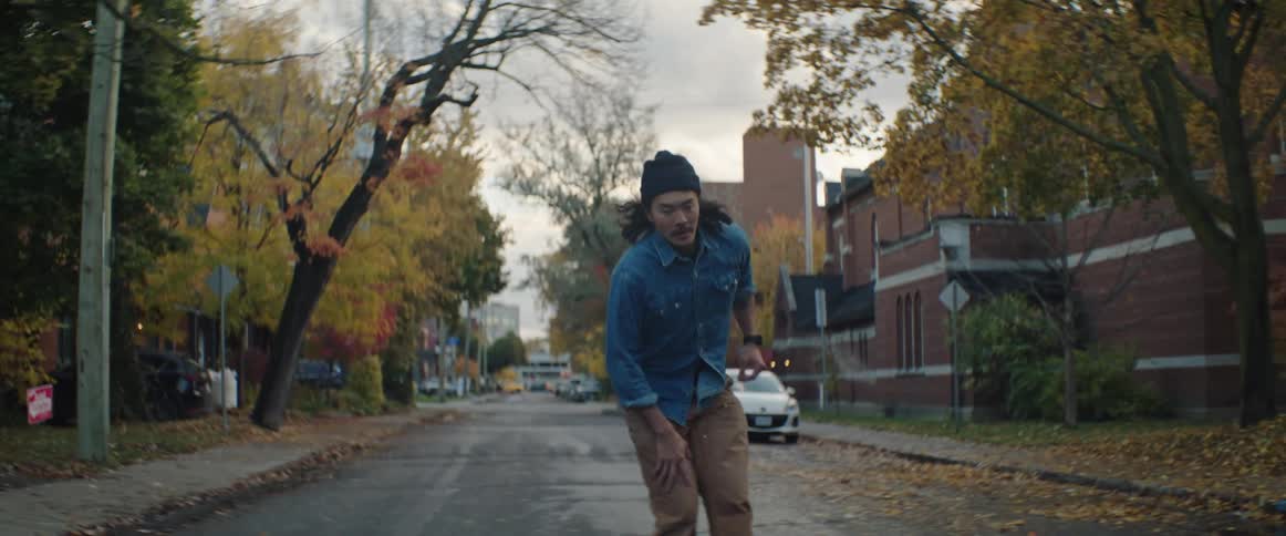 Man with long hair and moustache rides a skateboard on the town streets in the morning