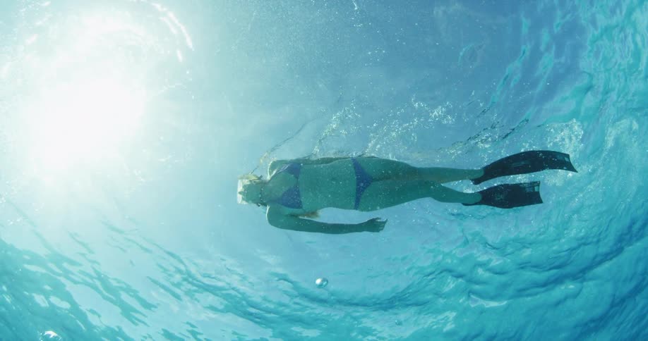A female diver is being filmed from underneath swimming along the surface