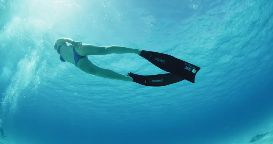 A woman wearing flippers and a bikini is swimming underwater