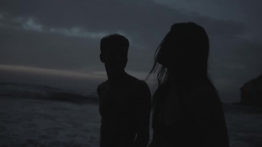 Couple walking and laughing on a beach in the early evening