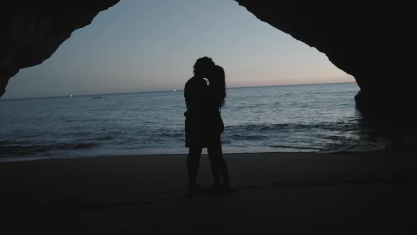 A man and woman approach each other and embrace on a beach at dusk