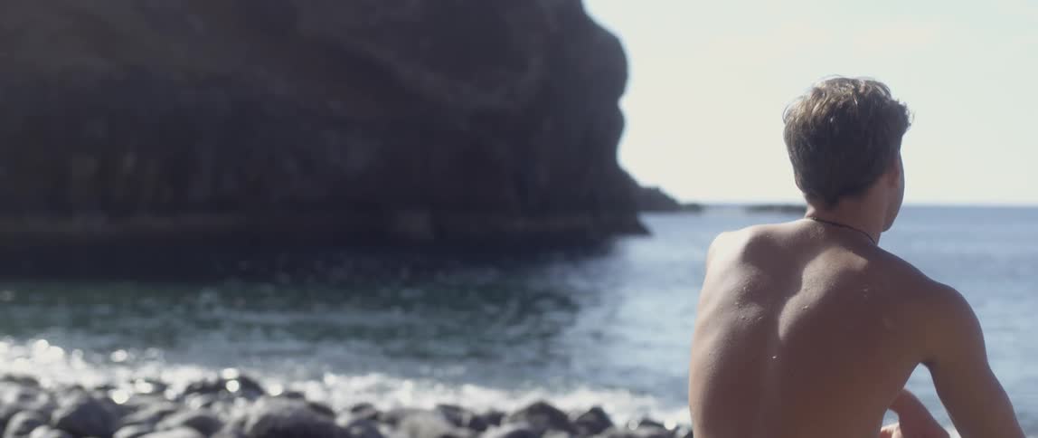 Young man sitting on a rocky beach on a clear day