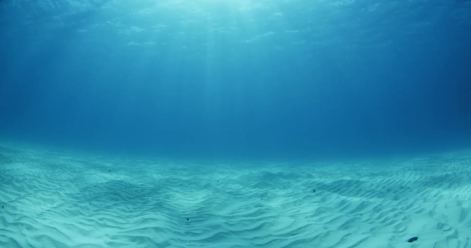 The sun is shining through the water on the sand underwater