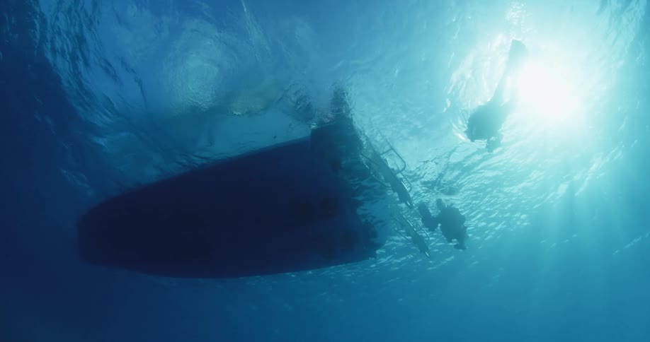 Divers and a boat are being filmed from underneath the ocean