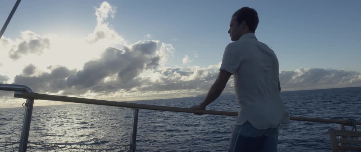 A man holds a boat railing as the boat travels across the water