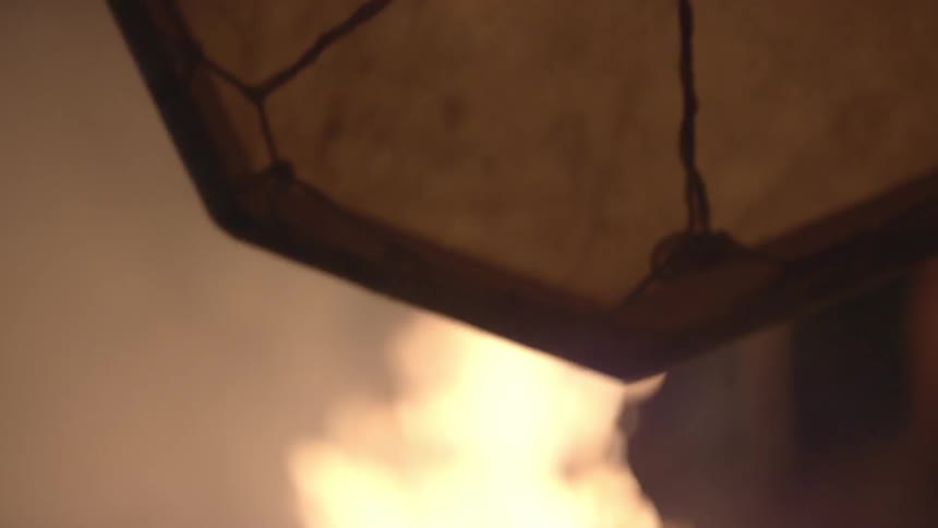 A man beating a drum as he stands next to a campfire