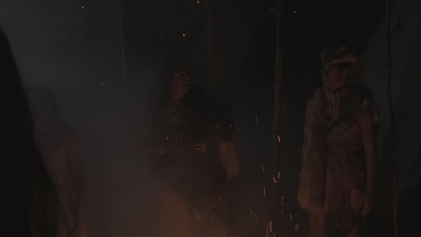 A group of people gather around a fire in the woods at night