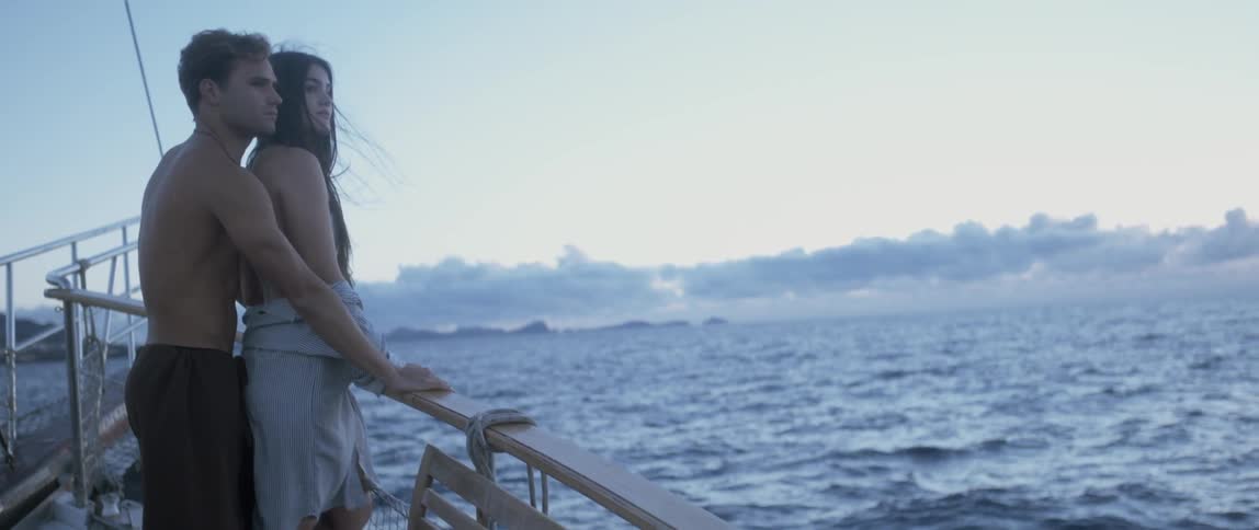 Couple standing on a ship's railing looking out at the ocean