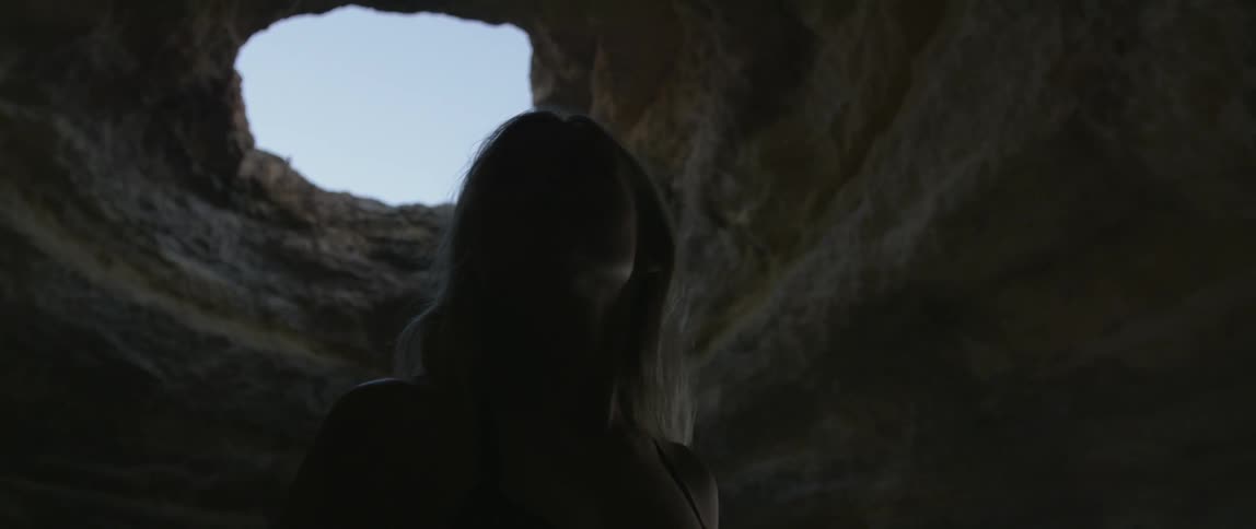 Woman standing in a cavernous area with a small hole of light above her
