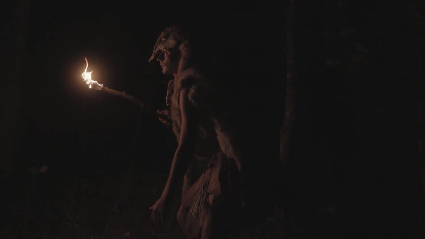 Tribal man walking through a dark area carrying a torch