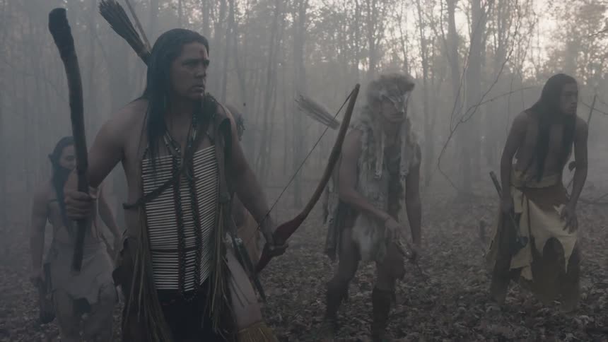 A native american hunting parting creeps cautiously through a misty forest