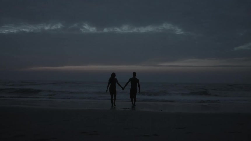 Couple walking towards the water on a beach in the early evening while holding hands
