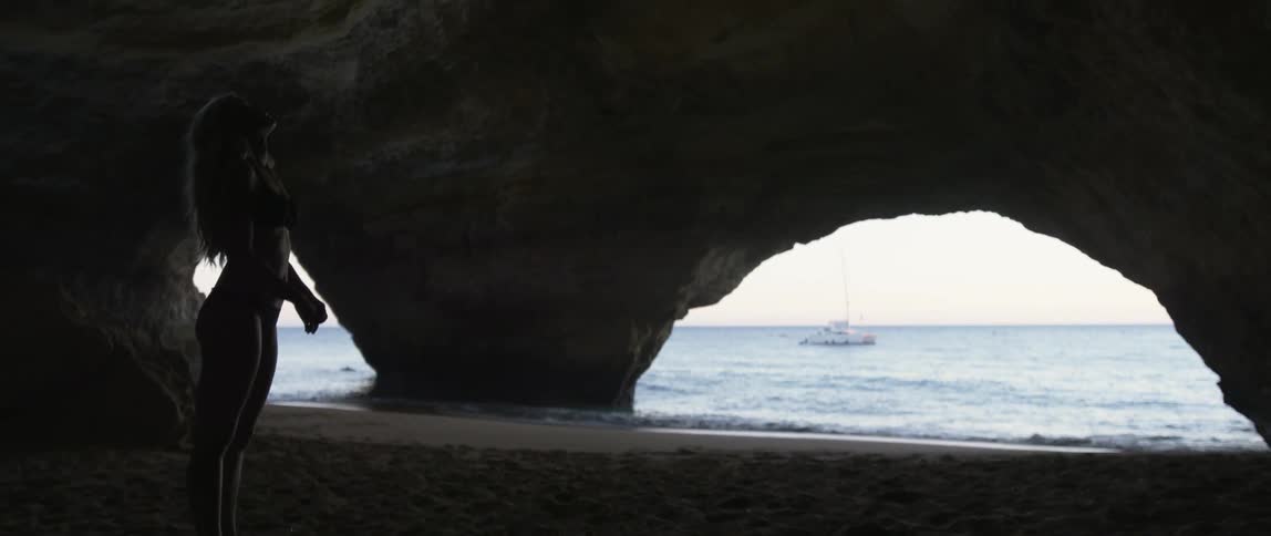 A woman stands in a cavernous rock formation at the beach
