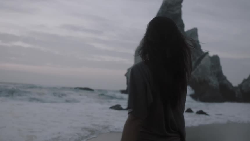 Woman walking towards the water's edge on a beach at sunset