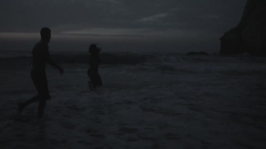 Two people are running along a beach playing in the water and with each other