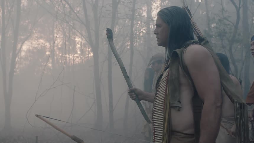 Native americans holding weapons stand in a misty forest and look around