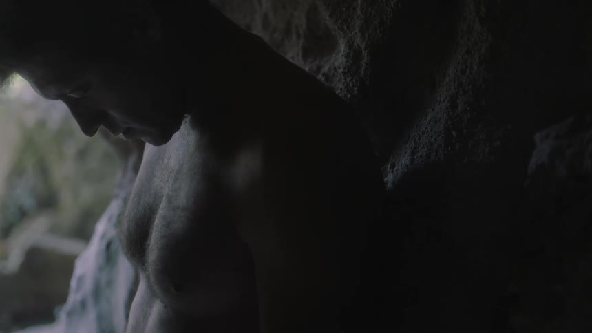 A man leans against a stone wall in the dark