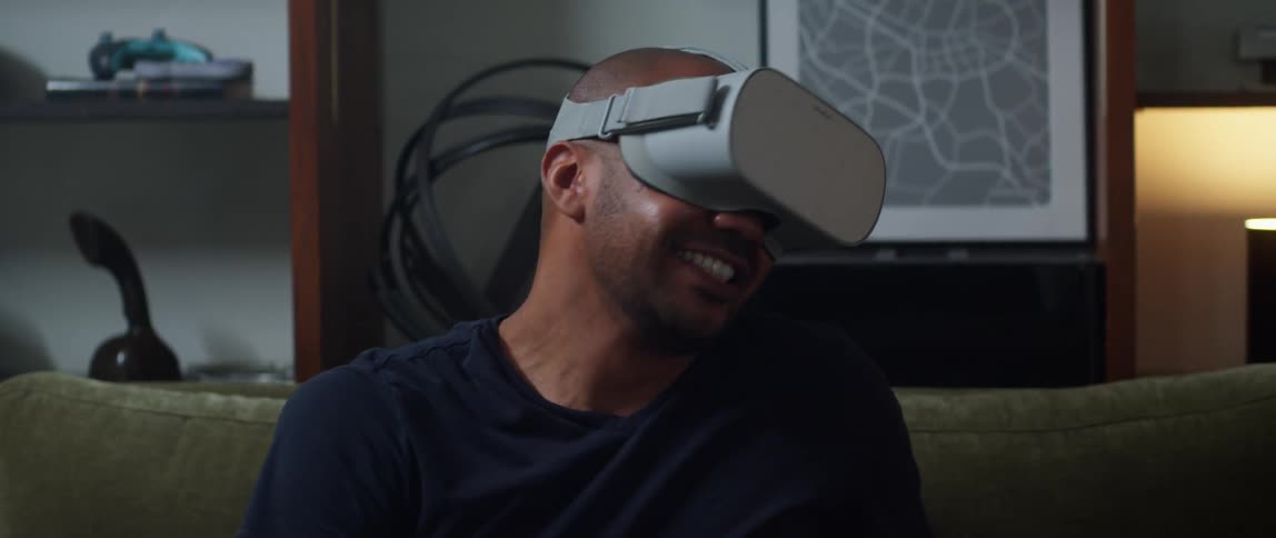 A man smiling and laughing while using a virtual reality headset on a living room sofa